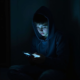 young man in a hoodies staring at his phone in a dark room